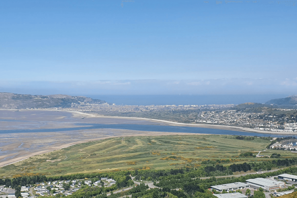 A panoramic view of a coastal town with a bay and distant hills under a clear blue sky.